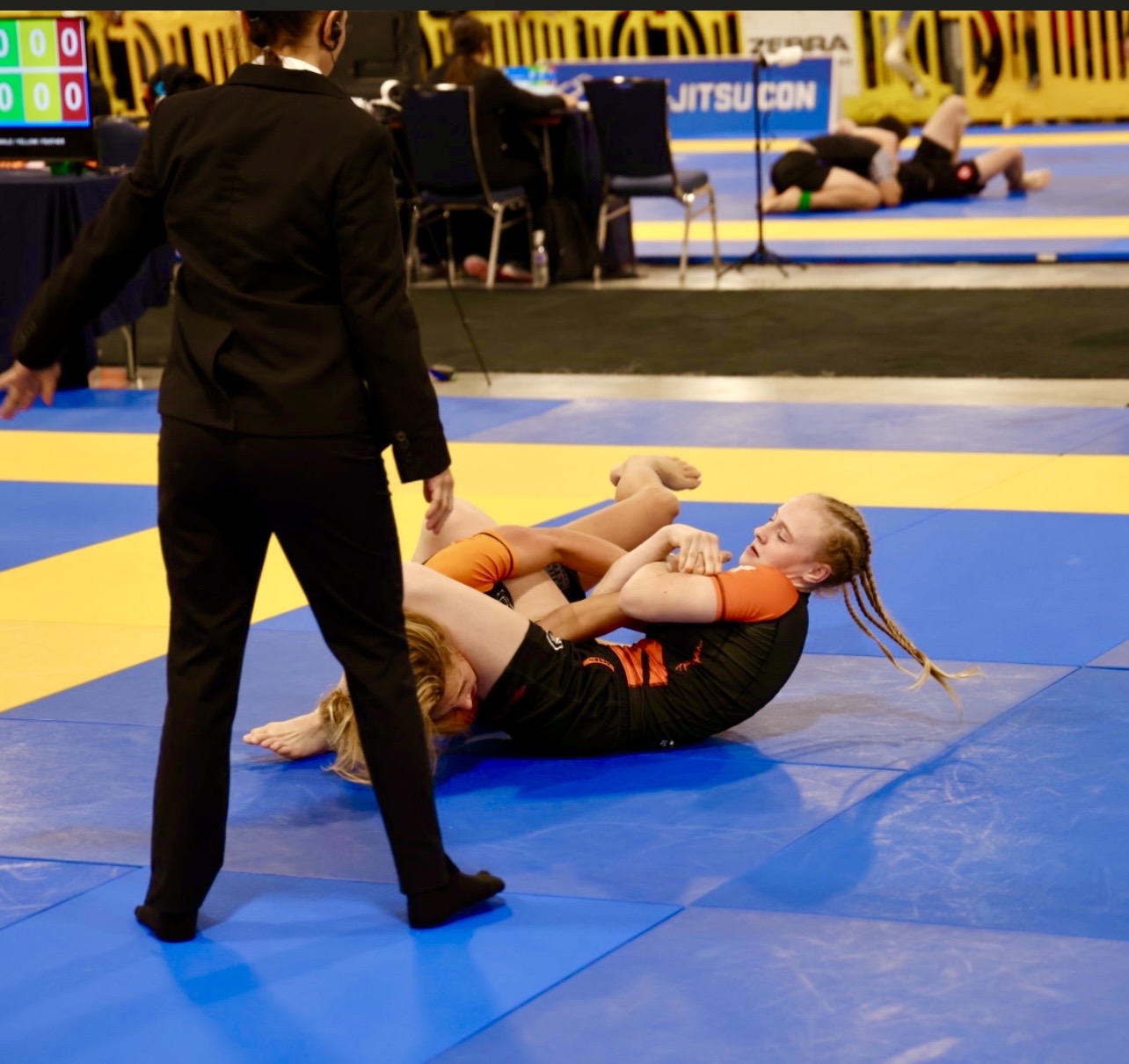 Keppnismynd úr keppnistöflu IBJJF Pan Kids No-Gi Championship 2024. Viðfangið er sýnt í yfirráðastöðu að ofan. Viðurkennt IBJJF keppnisumhverfi með stigaborði og aðliggjandi mottum sýnilegum í bakgrunni.